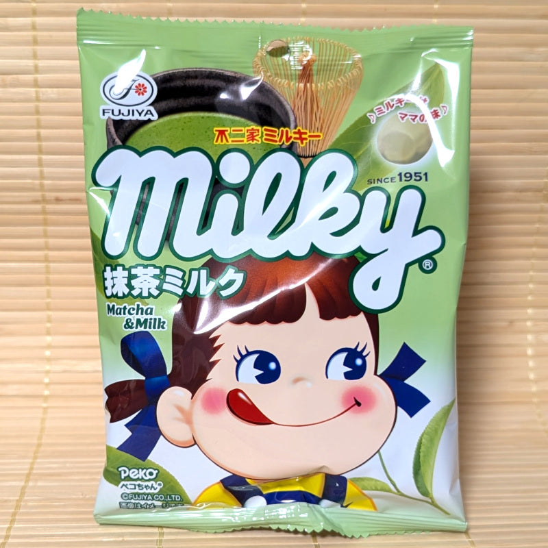 A pack of Fujiya Milky Matcha and Milk candies. Displayed on a tatami background. Peko Chan's cute big head is shown on the front of the bag.