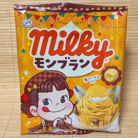 An orange and yellow 68g bag of Fujiya Milky Mont Blanc Candy featuring Peko-chan and a chestnut Mont Blanc cake graphic on a bamboo mat.