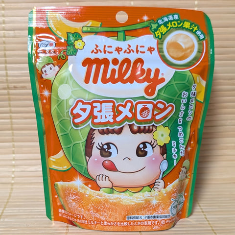 An orange and green 36g pouch of Fujiya Milky Hokkaido Yubari Melon candy showing Peko-chan in a melon hat and a slice of orange melon fruit on a tatami background.