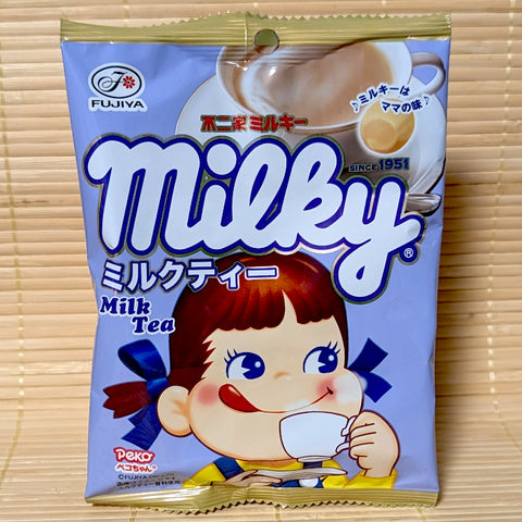 A light purple pouch of Fujiya Milky Milk Tea Soft Candy featuring Peko-chan sipping tea next to a teacup illustration on a bamboo background.