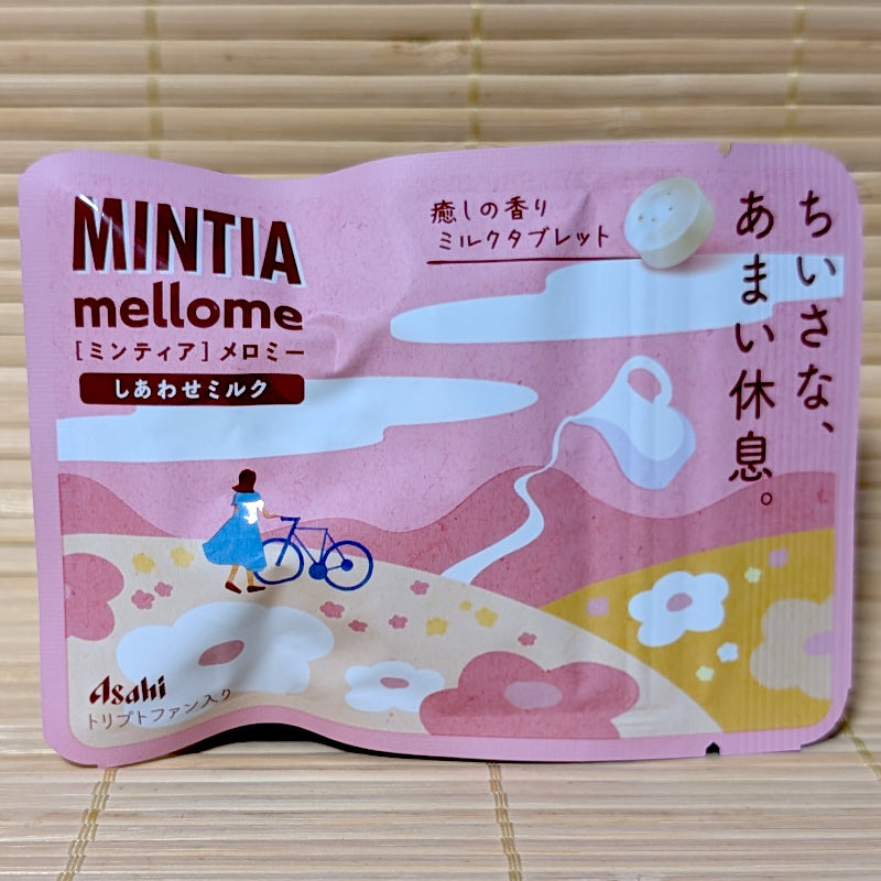 A soft pink matte foil pouch of Asahi Mintia Mellome featuring a minimalist drawing of a girl and a bicycle in a meadow, on a tatami background.