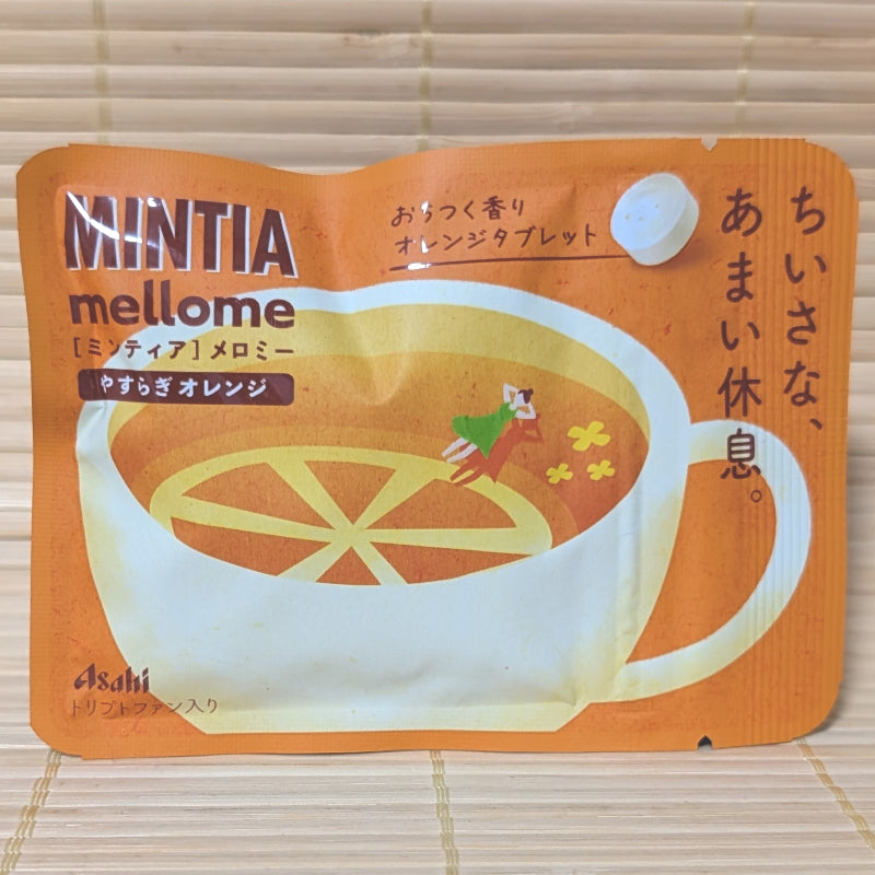 A soft orange matte foil pouch of Asahi Mintia Mellome featuring a whimsical drawing of a girl resting in a tea cup, on a tatami background.