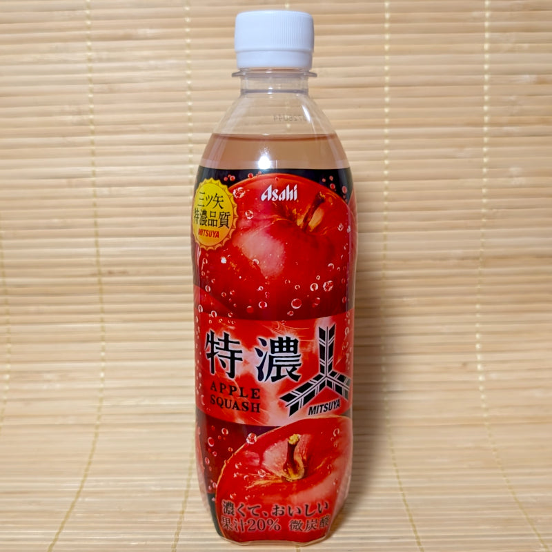 A 500ml PET bottle of Asahi Mitsuya Tokunou Apple Squash soda displaying bold red apple graphics on a bamboo mat background.