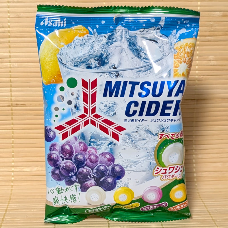 A blue and white bag of Mitsuya Cider Soda Hard Candy featuring ice splash, grape, lemon, and orange illustrations on a bamboo background.   