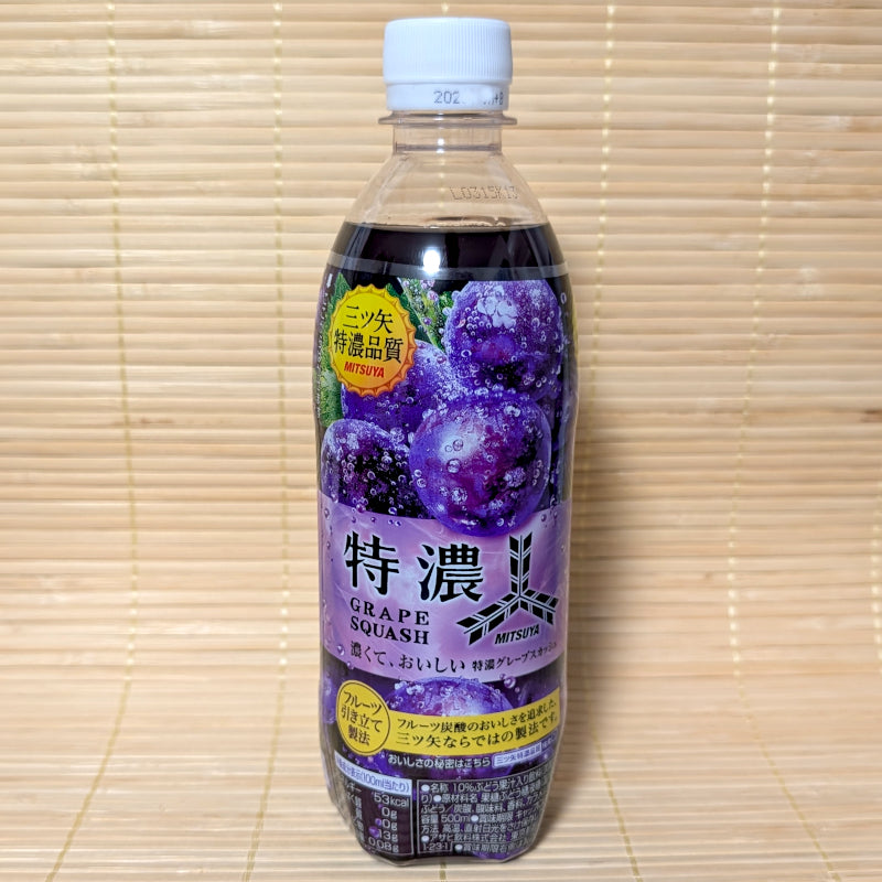A 500ml plastic PET bottle of Asahi Mitsuya Tokunou Grape Squash featuring a rich purple label covered in juicy grapes, on a tatami background.