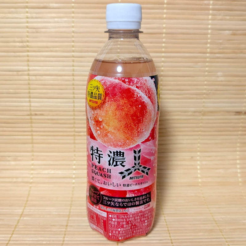 A 500ml plastic PET bottle of Asahi Mitsuya Tokunou Peach Squash with a vibrant red and pink label showing a plump, juicy peach, on a tatami background.