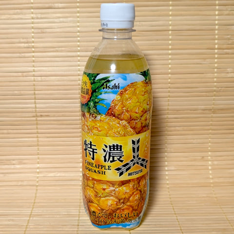 A clear plastic bottle of Asahi Mitsuya Fine Pineapple Squash soda showing rich yellow juice and large graphics of whole pineapples on a tatami background.