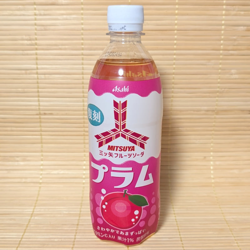 A 500ml plastic PET bottle of Asahi Mitsuya Plum Soda featuring a bright magenta label with a ripe plum graphic, on a tatami background.