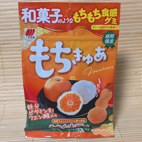 An orange and red pouch of Mochi-Cure Mikan Daifuku gummies displayed on a traditional tatami background.