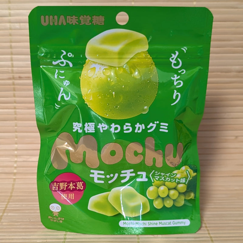 A green 45g pouch of UHA Mochu Shine Muscat Gummy featuring rectangular soft candies and grape illustrations on a bamboo mat.