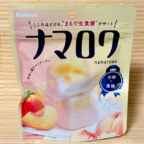 A pastel pink and yellow pouch of Kabaya Namarowa Gummy White Peach & Yellow Peach with fresh peach illustrations on a bamboo mat background.
