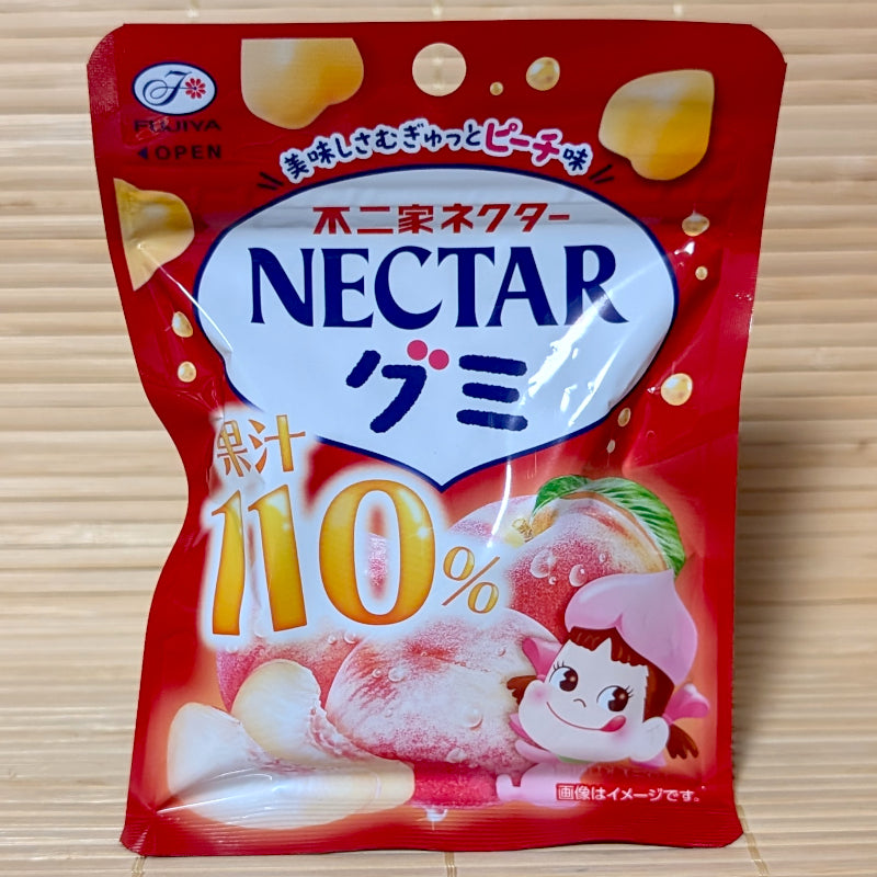 A bold red 54g resealable pouch of Fujiya Nectar 110% Peach gummies displaying white peach artwork and Peko-chan mascot graphics on a bamboo mat background.