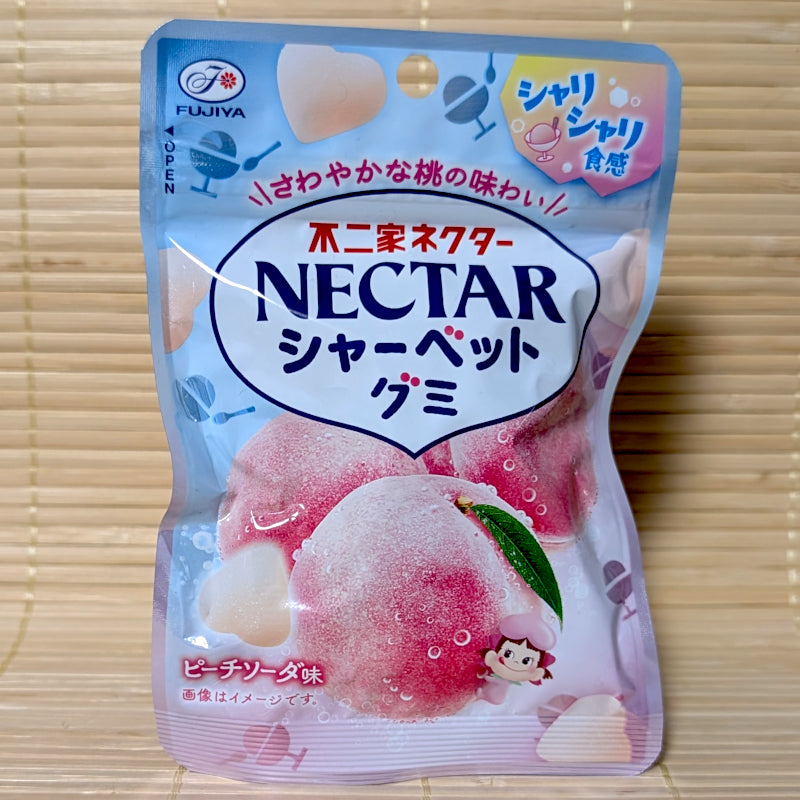 A light blue and pink pouch of Fujiya Nectar Sherbet Gummy Peach Soda showing frosted peaches, heart-shaped gummies, and Peko-chan on a tatami background.