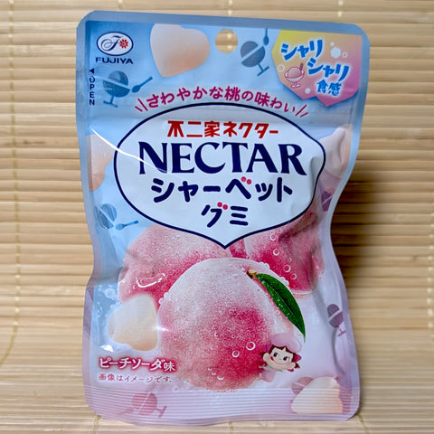 A light blue and pink pouch of Fujiya Nectar Sherbet Gummy Peach Soda showing frosted peaches, heart-shaped gummies, and Peko-chan on a tatami background.