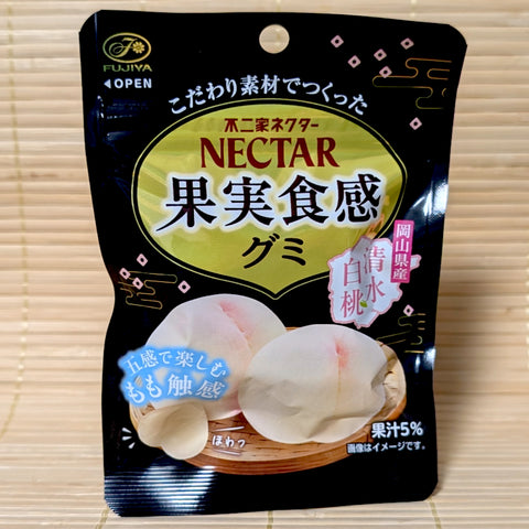 An elegant black and gold pouch of Fujiya Nectar White Peach gummies showing realistic whole fresh peach graphics on a tatami background.