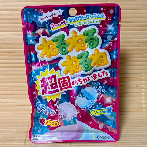 A vibrant pink and blue 21g pouch of Kracie Neru Neru Nerune Grape and Soda fizzy candy tablets on a bamboo mat.