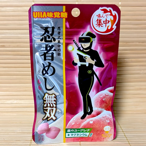 A metallic pink and silver 20g pouch of UHA Ninja Meshi Musou Peach gummies featuring a futuristic VR ninja standing on fresh pink peaches against a tatami background.