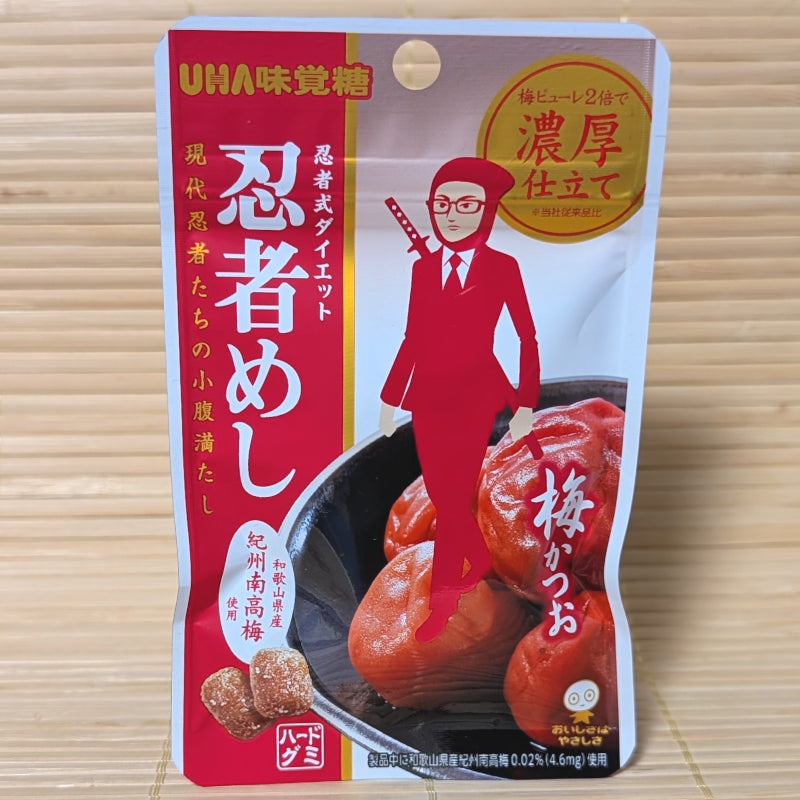 A white and red resealable pouch of Ninja Meshi Ume Katsuo gummies featuring a red ninja businessman, photographed on a tatami background.