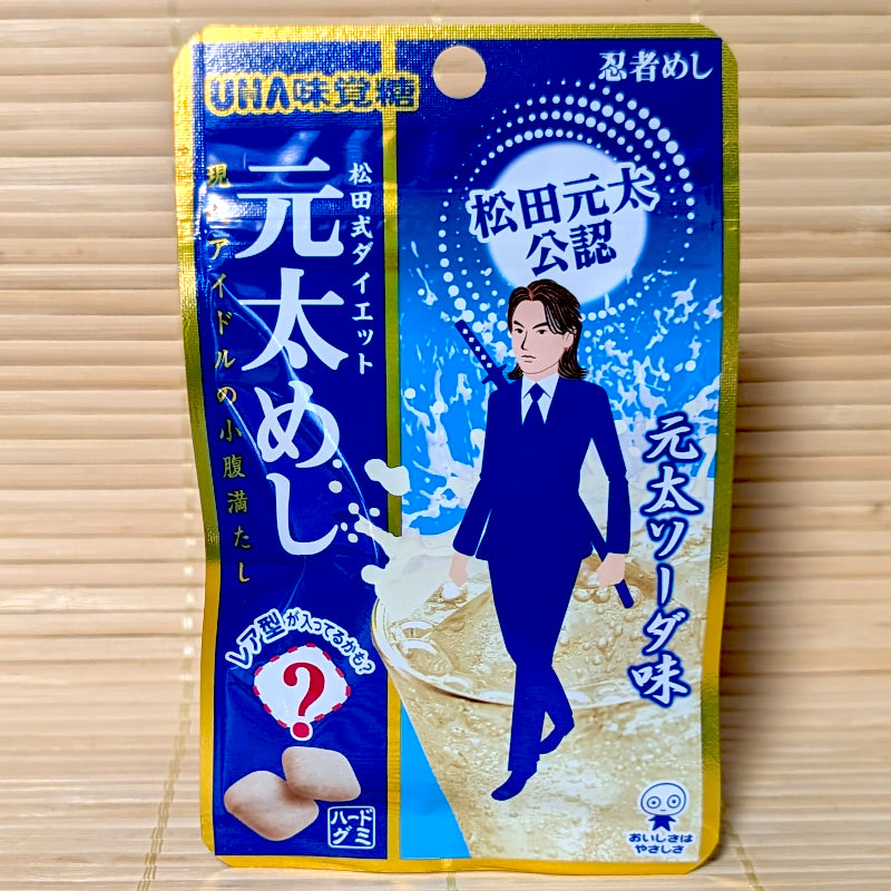 A blue and gold 20g pouch of Genta Meshi Genta Soda gummies featuring an anime illustration of Genta Matsuda on a bamboo mat background.