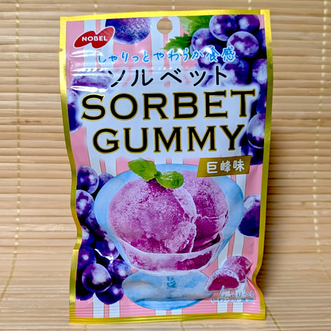 A pink and gold resealable pouch of Nobel Sorbet Gummy Kyoho Grape flavor showing a glass bowl of purple sorbet on a tatami background.