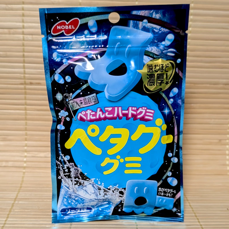 A metallic cosmic blue space themed pouch of Nobel Petagu White Soda gummy candy showing a flat blue alien graphic on a tatami background.