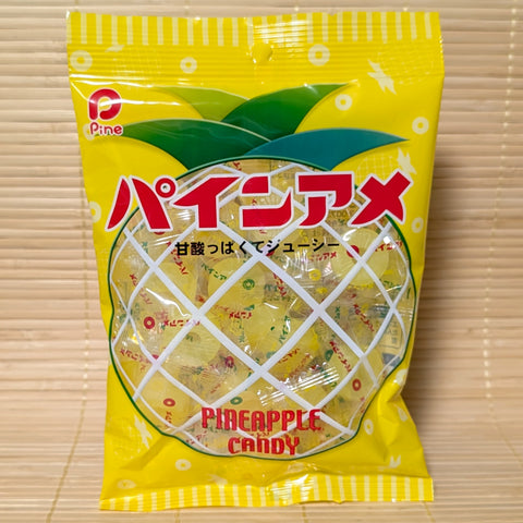A vibrant yellow 120g bag of Pine-Ame Pineapple Hard Candy showing individually wrapped golden ring candies inside a pineapple-patterned bag on a bamboo mat background.