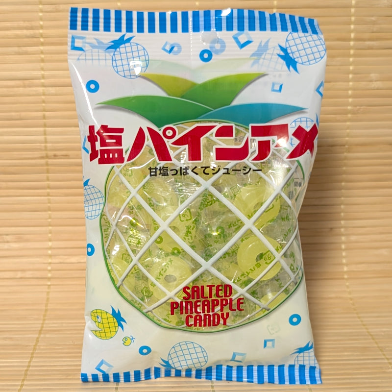 A white and blue striped bag shaped like a pineapple filled with individually wrapped yellow Pine Ame salty candy rings on a tatami background.