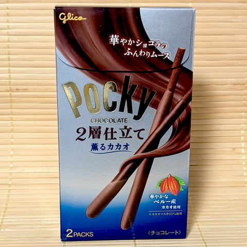 A silver and blue box of Glico Pocky Aromatic Cacao 2-Layer Mousse featuring two chocolate Pocky sticks and cacao pod graphics on a bamboo background.