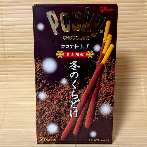 A dark brown box of Glico Pocky Winter Fuyu no Kuchidoke Cocoa featuring cocoa dusting graphics on a bamboo mat background.