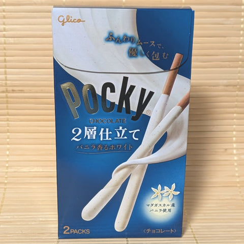 A deep blue box of Glico Pocky Vanilla White Chocolate 2-Layer Mousse featuring two white chocolate Pocky sticks on a bamboo background.   