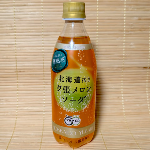A plastic PET bottle of Pokka Hokkaido Yubari Melon Soda with Japanese text on the label and a golden cap, placed on a bamboo mat background.

