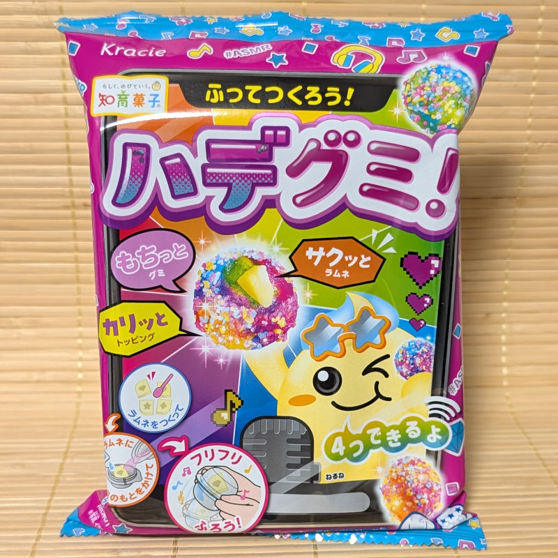 A bright purple and blue Kracie Popin' Cookin' Hade Gumi pouch on a tatami background showing a smiling sun character and colorful gummy balls.