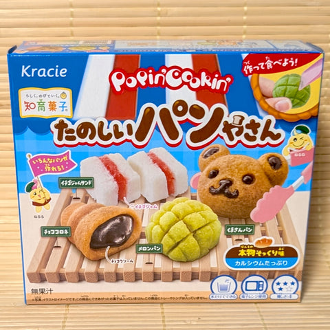 A box of Kracie Popin Cookin Tanoshii Bakery DIY Kit showing mini Bear Bread, Melonpan, Chocolate Cornet, and Strawberry Jam Sandwich resting on a bamboo mat.