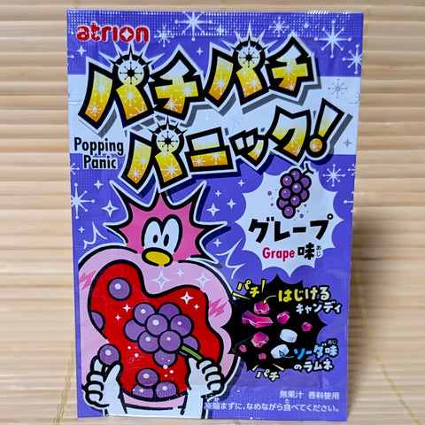 A small pack of grape soda popping candy by Atrion, a subsidiary of Meiji confectionery. The purple pack with cartoon images is displayed on a tatami background.
