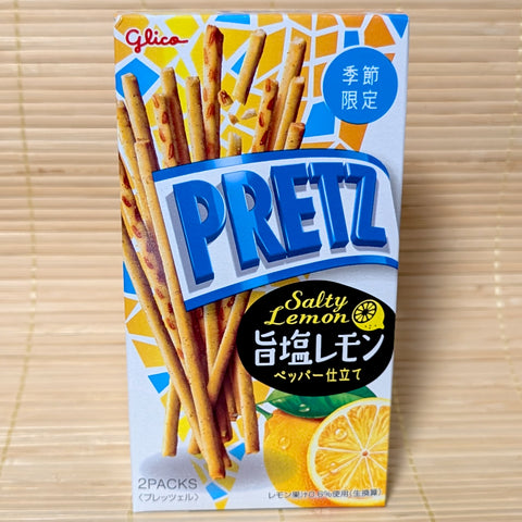 A blue and white Glico Pretz box on a tatami background featuring thin seasoned sticks and a sliced lemon with sea salt.