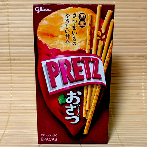 A deep red 62g box of Glico Pretz Osatsu sweet potato pretzel sticks featuring baked sweet potato graphics and sugar-coated sticks on a bamboo mat background.