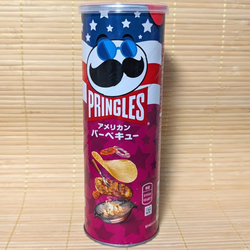 A tall purple and blue Pringles can with an American flag theme and an illustration of grilled meat and BBQ chips. Displayed on a tatami surface.