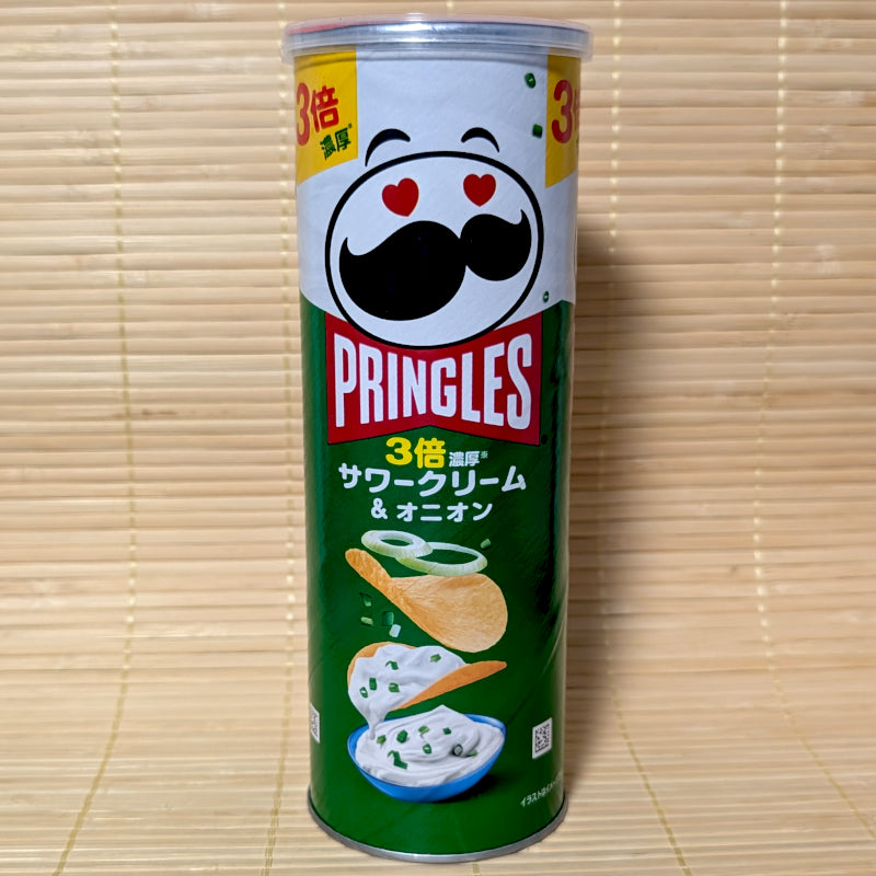 A green and white tall canister of Japanese Pringles Triple Sour Cream and Onion chips featuring the iconic mustache mascot with heart eyes, on a tatami background.