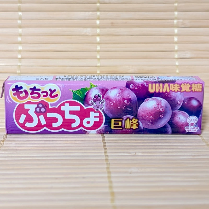 A purple UHA Puccho stick pack on a tatami background featuring large Kyoho grapes and the Puccho character.