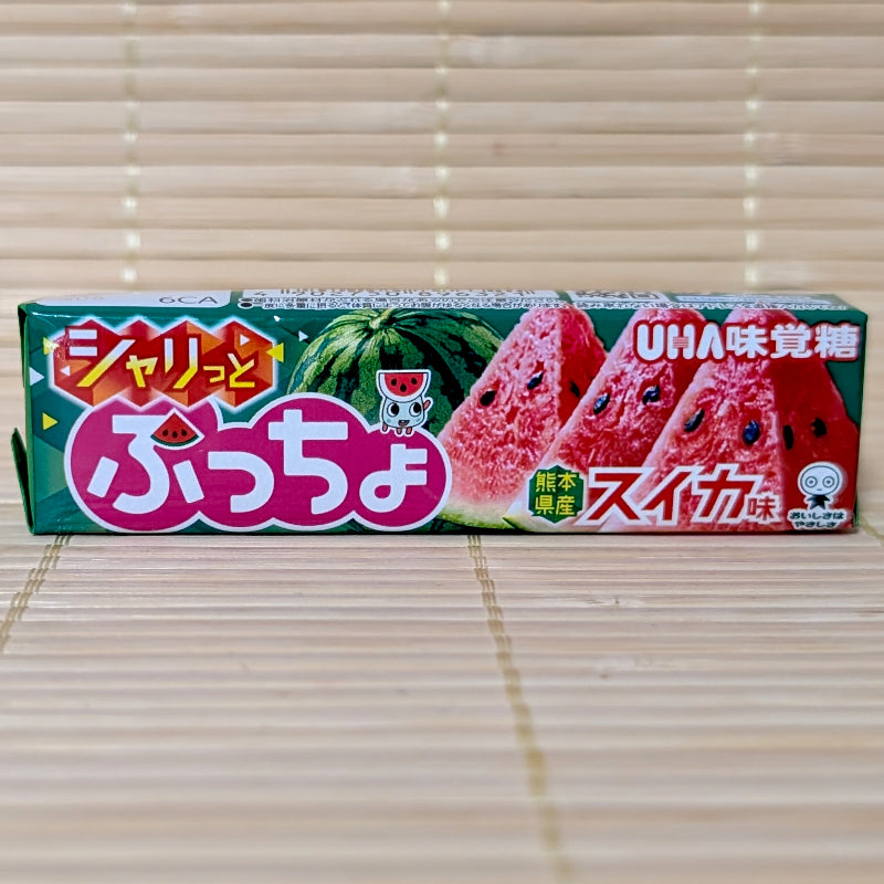 A green stick pack of UHA Puccho Suika Watermelon candy showing sliced red watermelons and a small mascot against a textured tatami background.