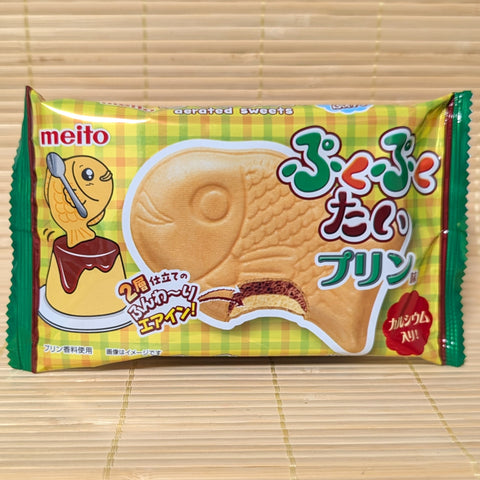 A yellow and green package of Meito Puku Puku Tai showing a fish-shaped wafer and a Japanese pudding graphic, on a tatami background.