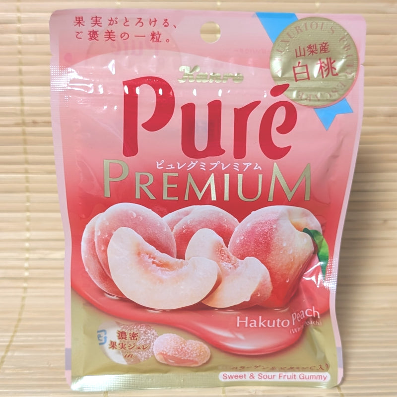 A light pink pouch of Puré Gummy Premium Yamanashi Hakuto White Peach featuring fresh peach graphics and a gold seal on a bamboo background.