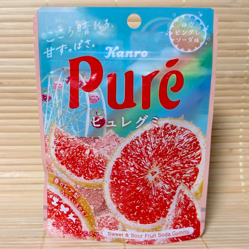 A light blue and pink resealable pouch of Kanro Pure gummies featuring large slices of pink grapefruit and a Ferris wheel in the background.