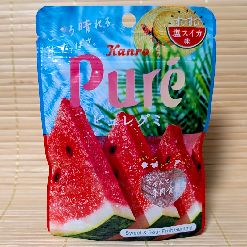 A blue and red pouch of Kanro Puré Salty Watermelon gummy showing large fresh watermelon slices, a straw hat, and a transparent heart window on a tatami background.