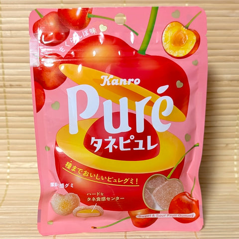 A bright pink 54g pouch of Kanro Puré Tane Puré Japanese Cherry gummies displaying cherry graphics and heart-shaped gummies on a bamboo mat.
