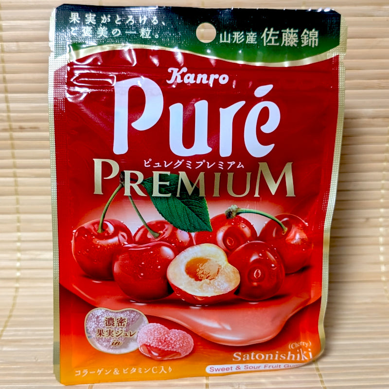 A bright red pouch of heart-shaped Kanro Puré Premium gummies featuring a liquid cherry center and Sato Nishiki cherries. Displayed on a tatami surface.