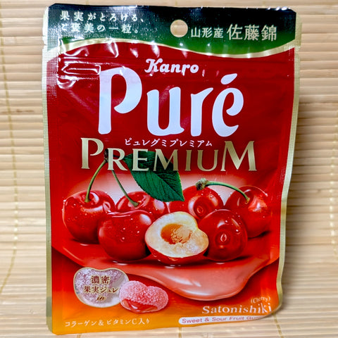 A bright red pouch of heart-shaped Kanro Puré Premium gummies featuring a liquid cherry center and Sato Nishiki cherries. Displayed on a tatami surface.