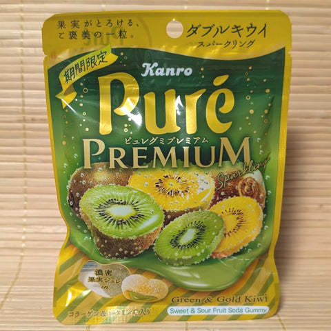 A metallic green and gold 54g pouch of Kanro Puré Premium Double Kiwi Sparkling gummies showing sliced green and gold kiwis, soda bubbles, and a cross-section of a heart-shaped gummy on a bamboo mat background.