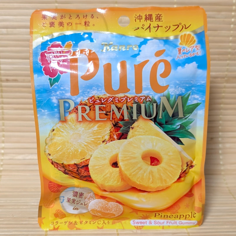 A bright yellow and blue beach-themed pouch of Kanro Pure Premium Pineapple gummy candy showing fresh cut fruit graphics on a tatami background.