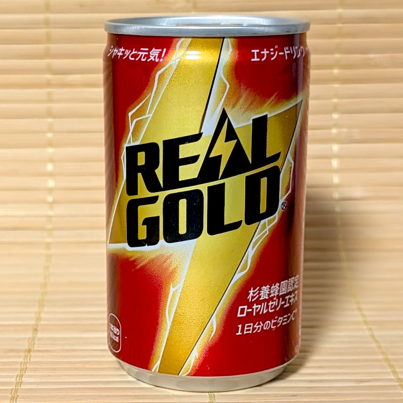 A red and gold 160ml steel can of Coca-Cola Real Gold Energy Drink showing lightning bolt graphics on a bamboo background.